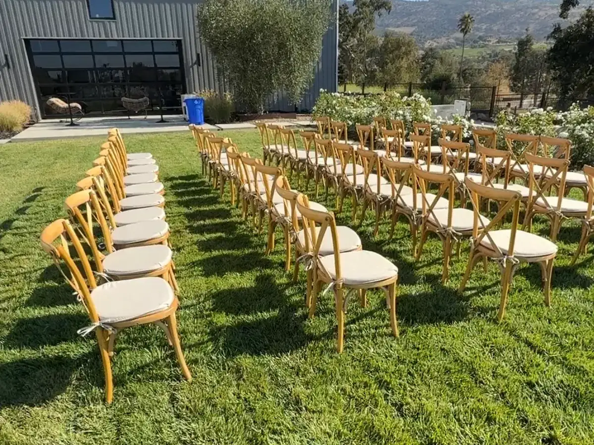 Rows of wooden cross-back chairs set up on a lawn for an outdoor ceremony