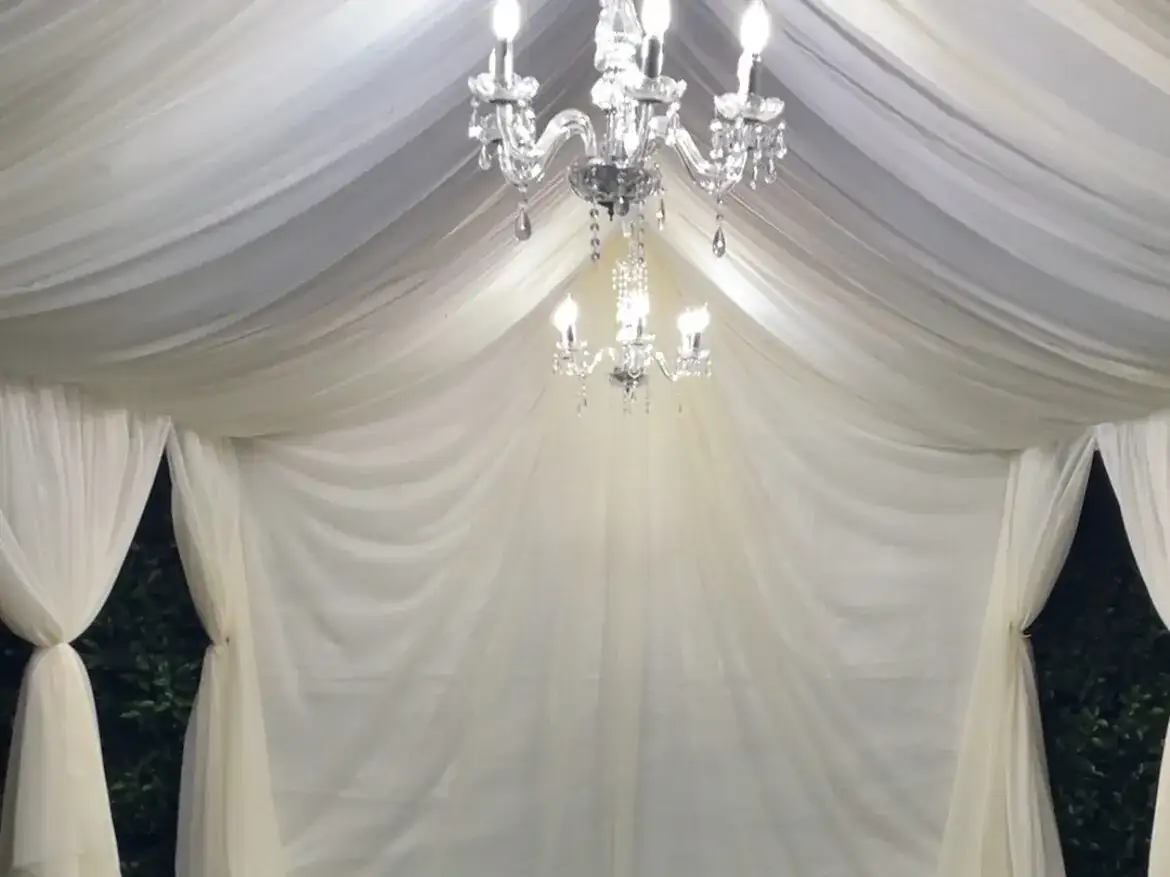 White draped tent glowing at night under a crystal chandelier
