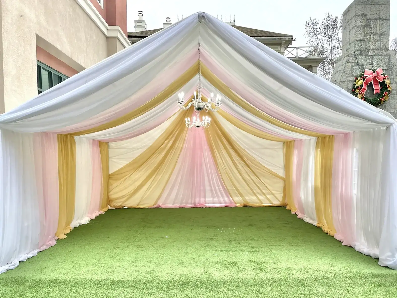 Tent entrance draped in blush and gold fabric with a crystal chandelier