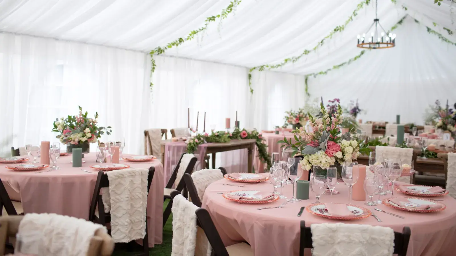 Reception tent draped in white with greenery garlands, blush tablecloths, and floral centerpieces