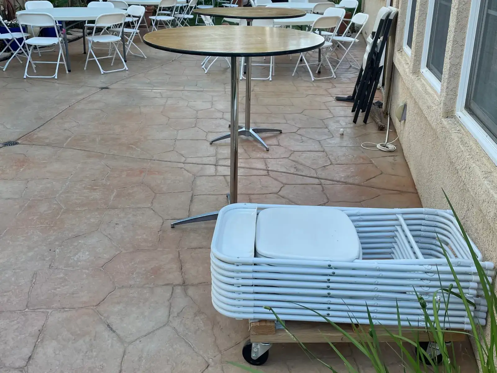 Patio mid-setup with cocktail tables, set tables, and a cart of stacked white folding chairs