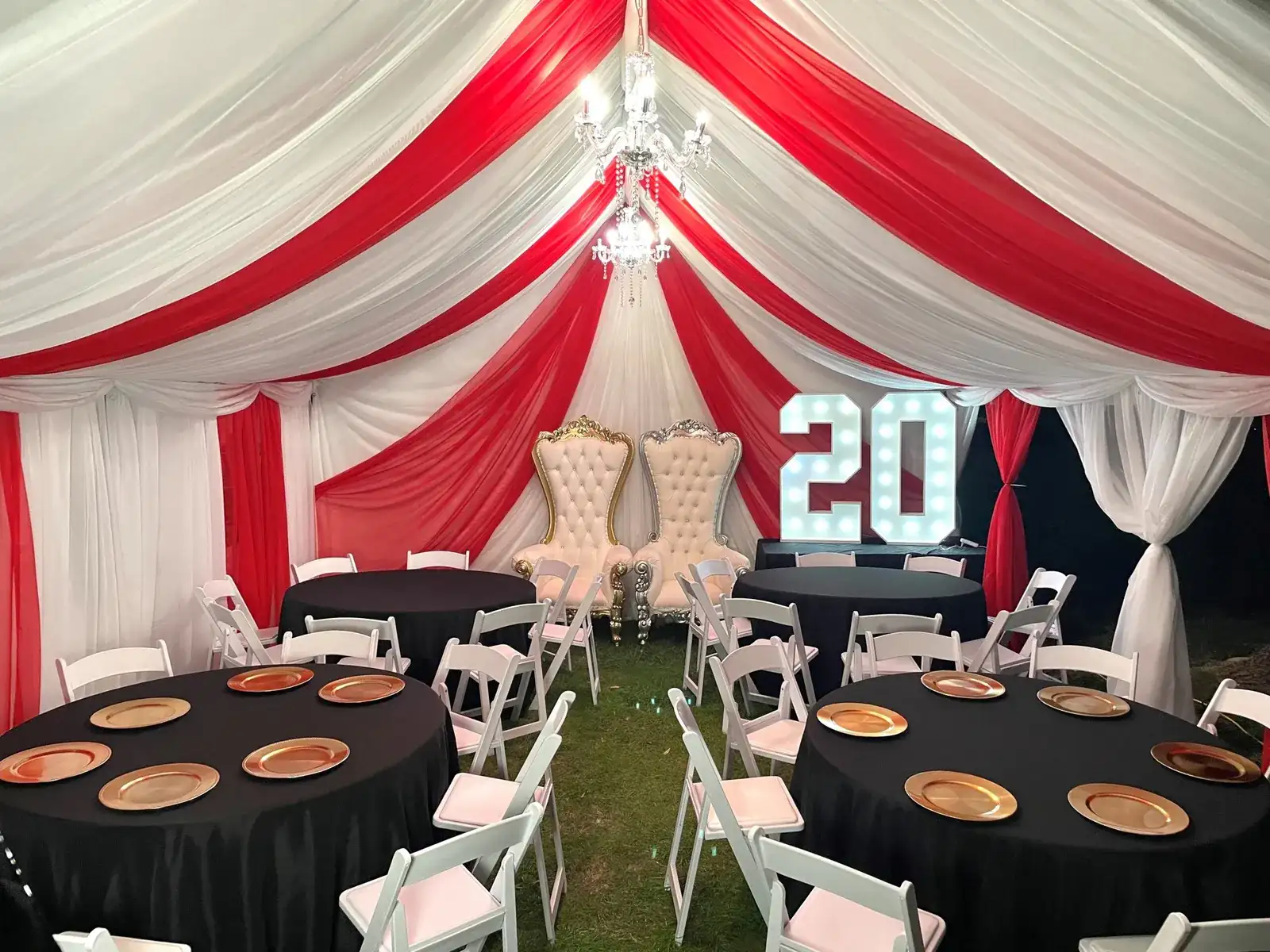 Tent draped in red and white with black round tables, throne chairs, and a lighted number 20 sign