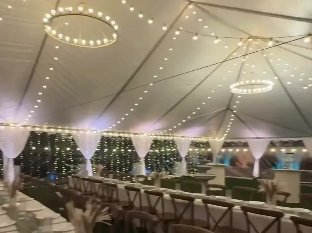 Evening tent lit with string lights and ring chandeliers over long farm tables