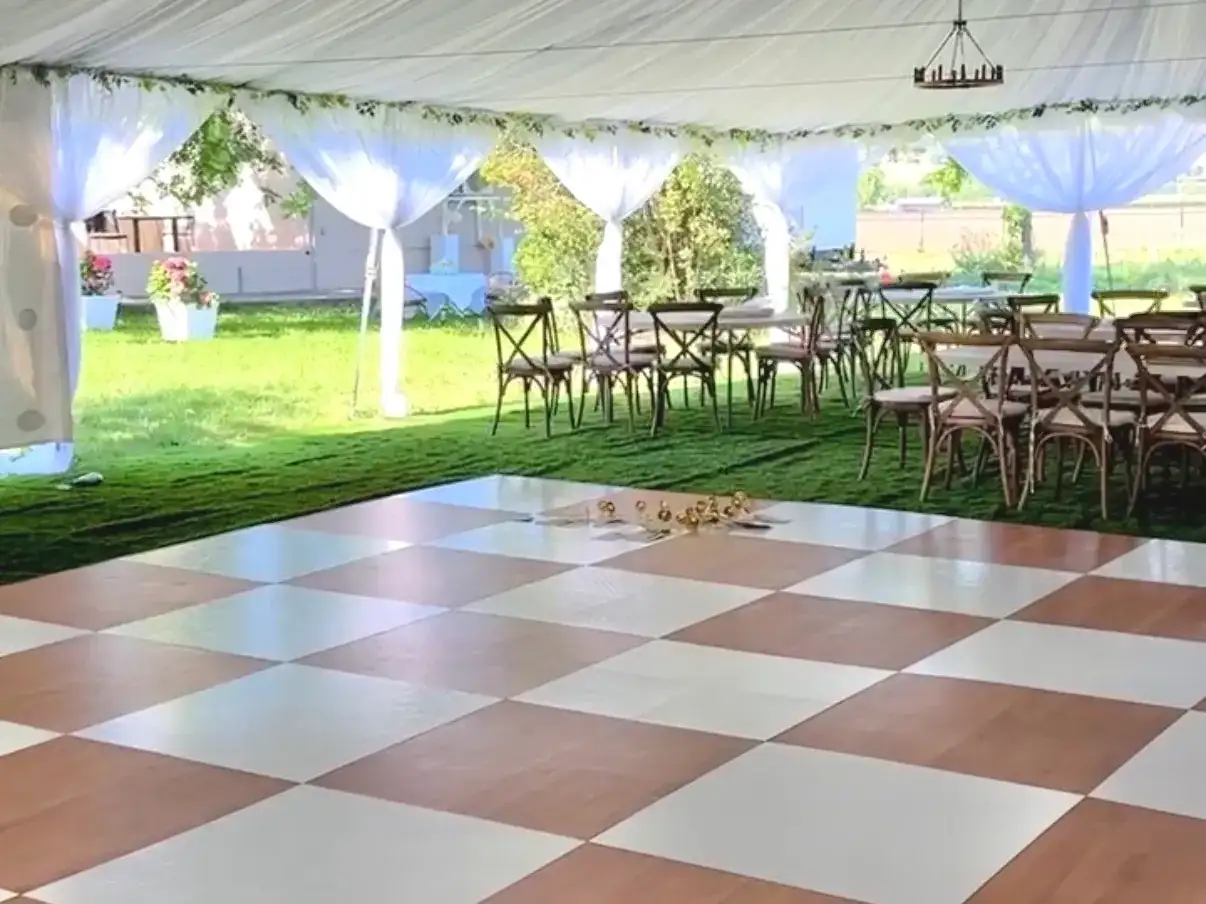 Checkered white and wood dance floor inside a draped tent with a round chandelier